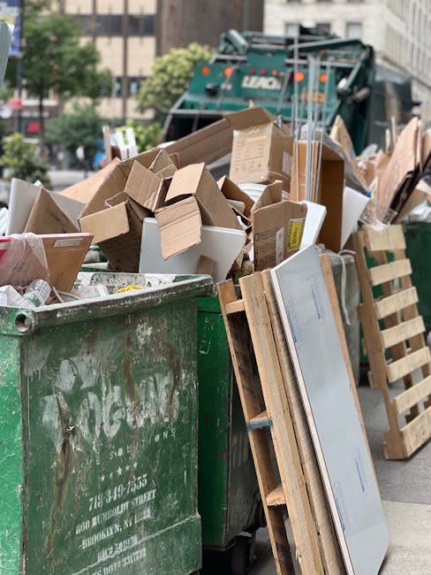 A large green wheeled waste bin is filled with a variety of discarded packaging materials, including cardboard boxes, some flattened and some partially intact, along with white and brown paper packagi