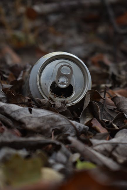 A large green wheeled waste bin is filled with a variety of discarded packaging materials, including cardboard boxes, some flattened and some partially intact, along with white and brown paper packagi